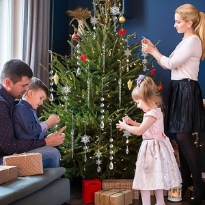 Family decorating Christmas tree with transparent acrylic snowflake and crystal ornaments