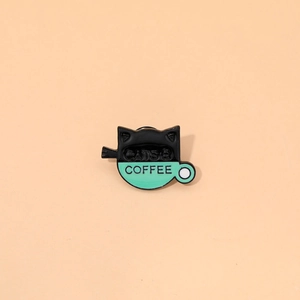 Macro shot of an enamel cat pin featuring a black cat and coffee cup with text detail