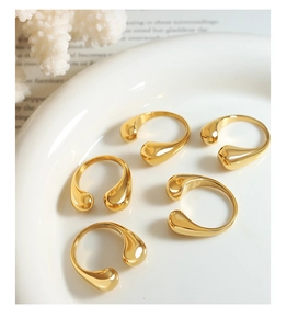 Detailed view of five polished 18k gold plated water drop rings in a ceramic bowl
