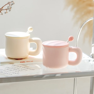 Minimalist ceramic mugs in cream and pink with matching lids and spoons on a glass shelf
