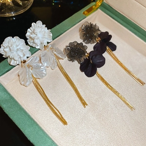 Detail view of pearl white and black acrylic petal tassel earrings in a jewelry box
