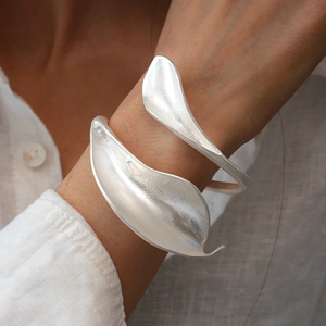 Close-up of matte silver open cuff bracelet with artistic leaf pattern on female wrist