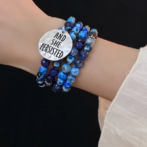 Detail shot of multi-layer blue beaded bracelet with engraved metallic pendant on wrist