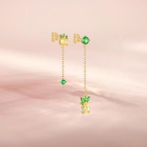 Detailed view of gold pineapple earrings with yellow and green crystals on pink background
