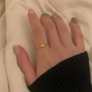 Close-up of minimalist gold S925 silver heart ring worn on a finger with warm background