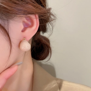 Close-up of minimalist beige enamel bean earrings on model with gold plating finish