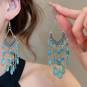 Detailed close-up of blue tassel earrings with silver chains and bead drops on a model