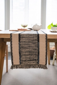 Close-up of woven table runner featuring beige and grey patchwork with tassel details