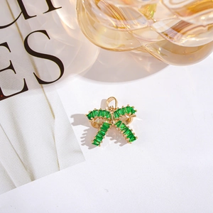 Detailed view of a gold bow pendant with green zircon stones on a white background