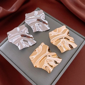 Detail of irregular square stud earrings in gold and silver with crumpled metal texture