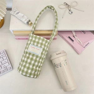 Quilted green plaid fabric water bottle bag with handle shown in a lifestyle desktop setting