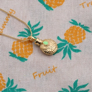Detail shot of a golden bottle pendant necklace with green enamel on a pattern cloth