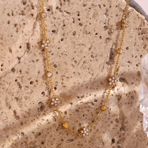 Close-up of golden chain necklace with white crystal flowers and round zircon accents