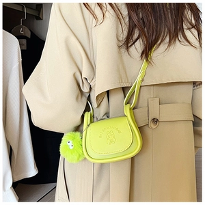 Lime green mini crossbody bag with cartoon embossed design and pompom charm on a trench coat