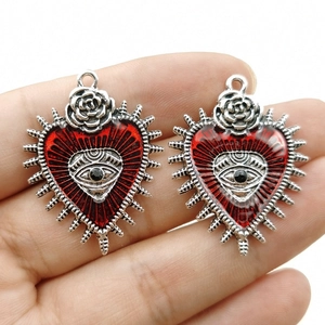 Gothic punk heart pendant with blood red eye and silver rose detail held in hand