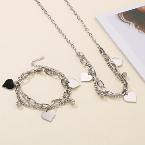 Detailed view of silver heart charms on layered stainless steel chain necklace and bracelet