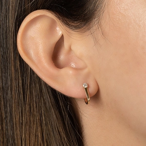 Close-up of a gold U-shaped earring with a clear zircon stone on a female ear