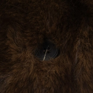 Détail de la texture en fausse fourrure marron foncé et du bouton rond sur la veste