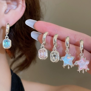 Close-up of sparkling star pendants and square crystals on silver huggie earrings