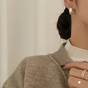 Close-up of minimalist silver C-shaped earrings and classic anchor link ring on a model