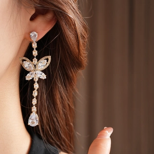 Detail of elegant gold butterfly drop earrings with clear zircon on a model's ear