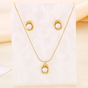 Macro detail of gold necklace and pearl earrings set on a white marble background