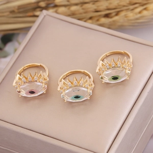 Three gold evil eye rings with colorful zircon inlays on a beige jewelry box