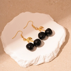 Dark style black resin cherry earrings with golden leaf hooks on a stone base