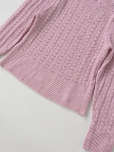 Close-up of pink knit top featuring delicate openwork wave patterns and ribbed cuffs