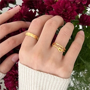 Detail of twisted knot and wavy gold rings on finger with floral background