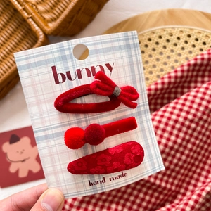 Close-up of three red fabric hair clips with velvet bow and floral embroidery on card