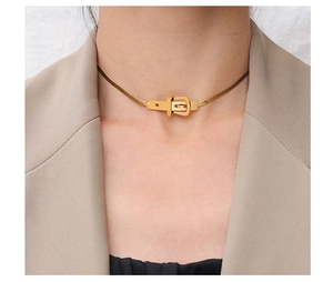 Close-up of gold belt buckle pendant necklace on a snake chain worn by a female model