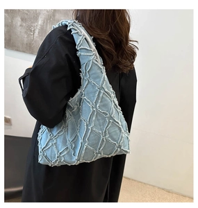 Close-up of light blue denim tote with quilted diamond pattern and fringe detail