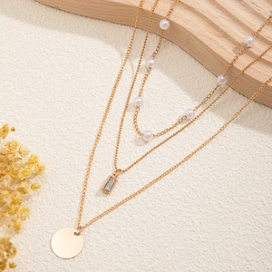 Detailed view of triple-layered gold necklace with faux pearls and geometric pendants
