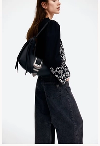 Detailed view of a black leather crossbody bag featuring metal hardware and fringe details
