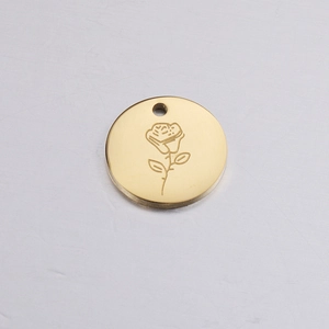 Macro shot of circular gold pendant featuring detailed rose flower engraving and hanging loop