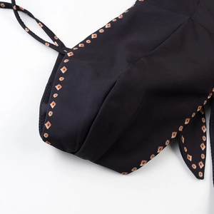 Detail shot of black dress fabric with orange diamond patterns and precise stitching