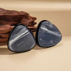 Detail of geometric resin triangle earrings with dark marble texture on warm background