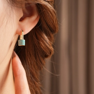 Detail of gold cylindrical earring featuring turquoise beads on a model's ear