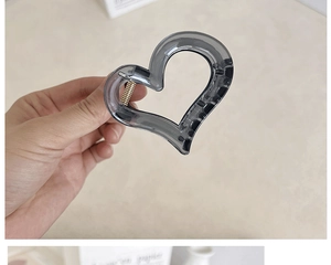 Detail of a translucent smoke grey heart hair claw clip with golden metal spring