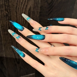 Detail of dark blue cat-eye press-on nails with blue butterfly sequins and stiletto shape