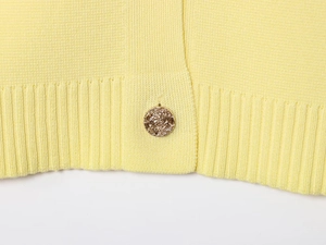 Close-up of yellow knit cardigan featuring textured golden metal button and ribbed hem