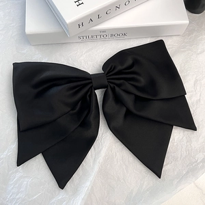 Detailed view of elegant black layered satin bow hair clip on a minimalist background