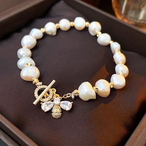 Macro detail of Baroque pearl bracelet featuring a zircon bee charm and gold OT clasp