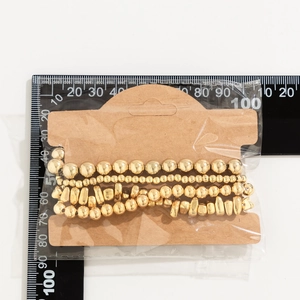 Detail showing golden beaded heart bracelet set on kraft paper card with ruler for scale