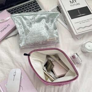 Flat lay of velvet cosmetic bags in silver and pink with toiletries on white bedding