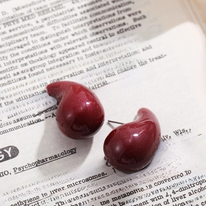 Close-up of dark red teardrop enamel stud earrings on vintage book page background