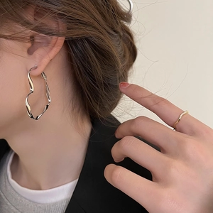 Détail de créoles en cœur argentées et d'une bague vague dorée sur un mannequin