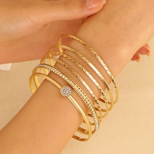 8-piece gold bangle set with diamond-studded details and textured patterns on model