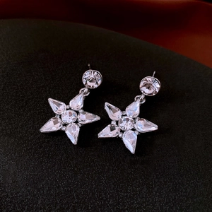 Macro detail of silver star earrings with sparkling rhinestones on dark fabric background